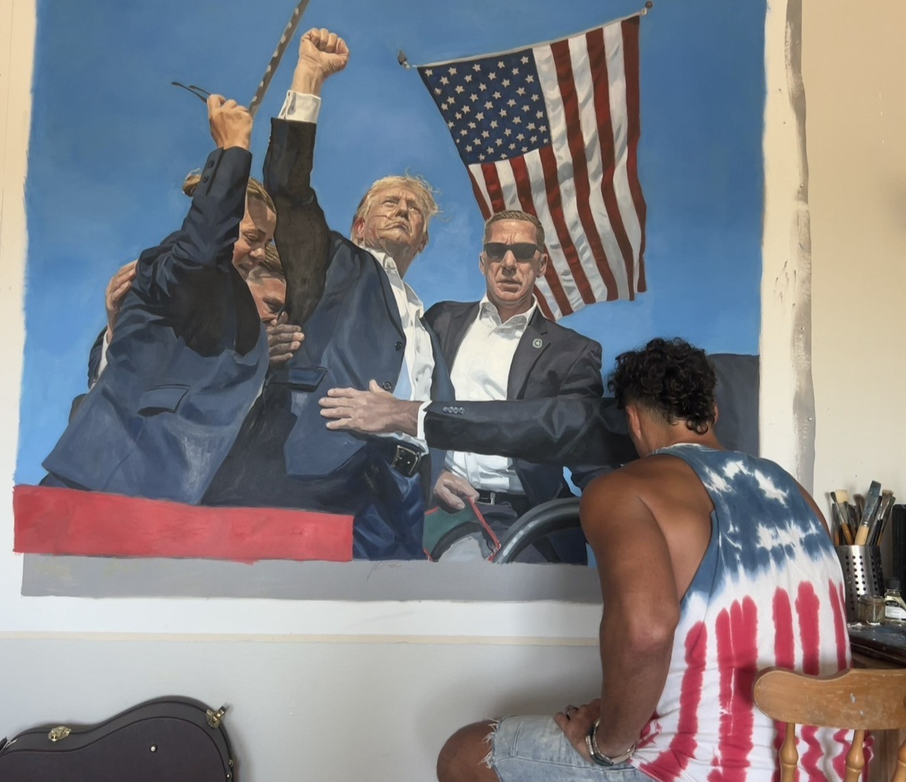 Chad H. Vivas painting a large canvas of a flag-lit crowd scene in his studio